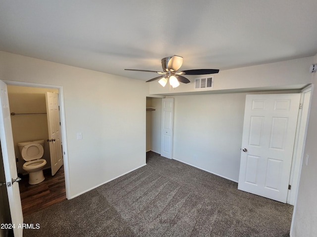 unfurnished bedroom with ensuite bath, dark carpet, and ceiling fan