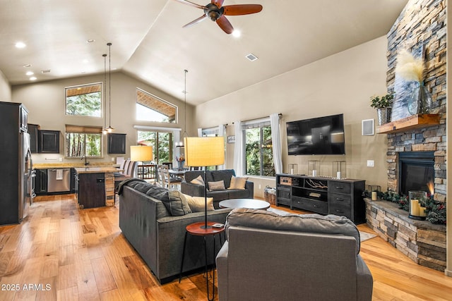 living room with visible vents, ceiling fan, light wood-style flooring, a fireplace, and high vaulted ceiling