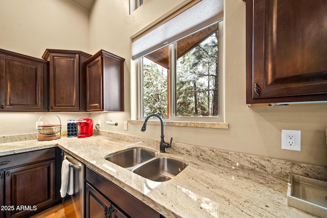 kitchen with a sink, light stone counters, and dark brown cabinetry