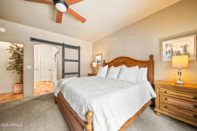 carpeted bedroom with a barn door, arched walkways, ceiling fan, and vaulted ceiling