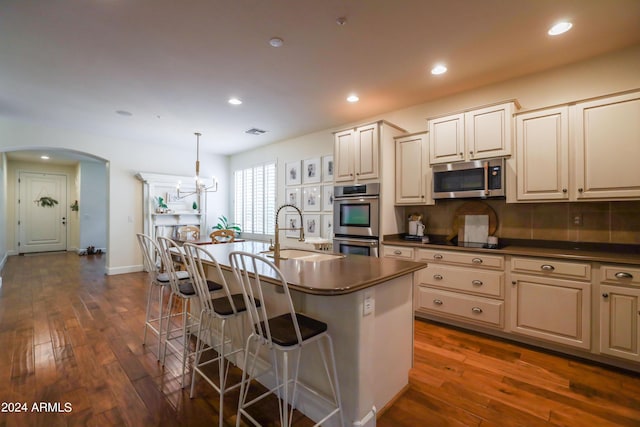 kitchen with a breakfast bar, sink, hanging light fixtures, a center island with sink, and appliances with stainless steel finishes