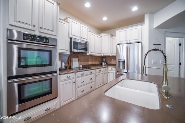 kitchen with tasteful backsplash, stainless steel appliances, sink, and white cabinets