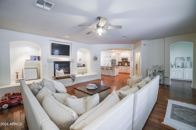 living room featuring built in shelves, dark hardwood / wood-style floors, and ceiling fan