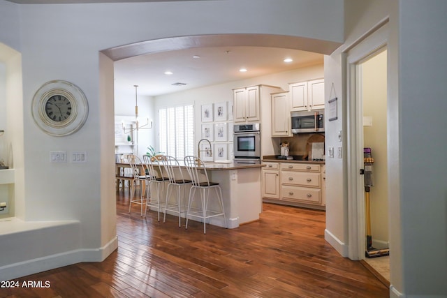 kitchen with appliances with stainless steel finishes, dark hardwood / wood-style floors, decorative light fixtures, a kitchen breakfast bar, and a center island with sink