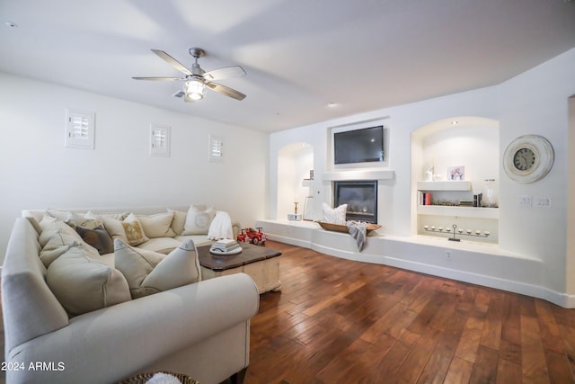 living room featuring dark hardwood / wood-style flooring, built in shelves, and ceiling fan