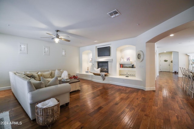 living room featuring built in shelves, dark wood-type flooring, and ceiling fan