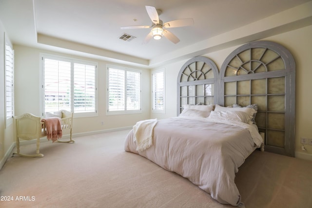 bedroom with ceiling fan, a raised ceiling, and light carpet