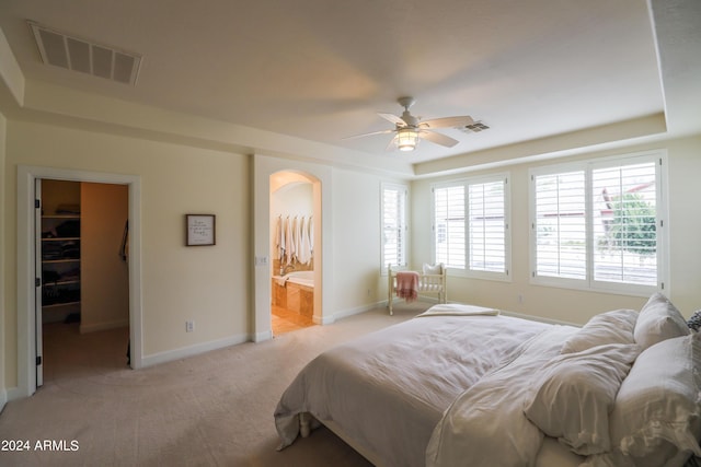 bedroom with a walk in closet, light colored carpet, connected bathroom, and a tray ceiling