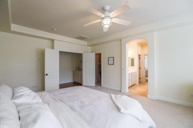 bedroom with ensuite bathroom, light carpet, and ceiling fan