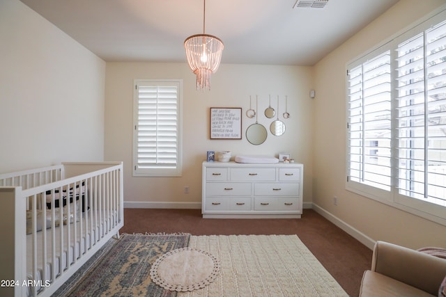 bedroom featuring multiple windows, a nursery area, a chandelier, and dark colored carpet