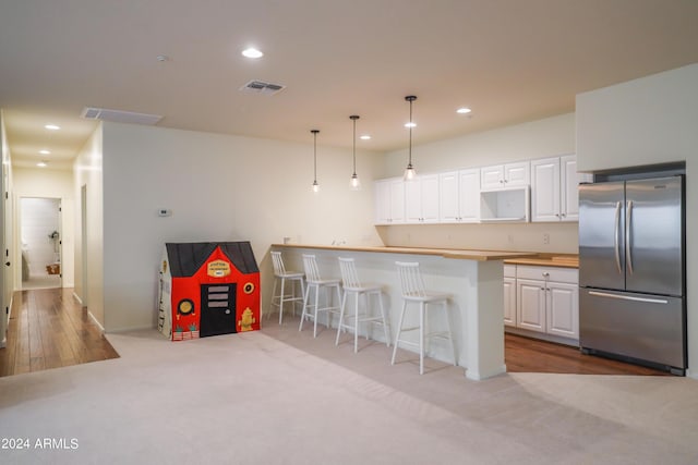 kitchen featuring pendant lighting, stainless steel fridge, a breakfast bar area, white cabinetry, and kitchen peninsula