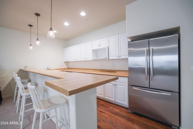 kitchen featuring a breakfast bar, stainless steel refrigerator, white cabinets, wooden counters, and hanging light fixtures