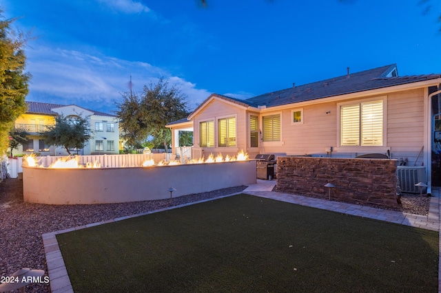 back house at dusk with cooling unit, a yard, and a fire pit