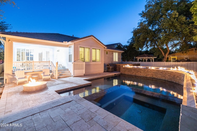 pool at dusk with a fire pit, a patio, and an in ground hot tub