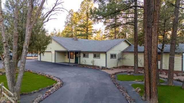 ranch-style house with aphalt driveway, a garage, roof with shingles, and a front yard