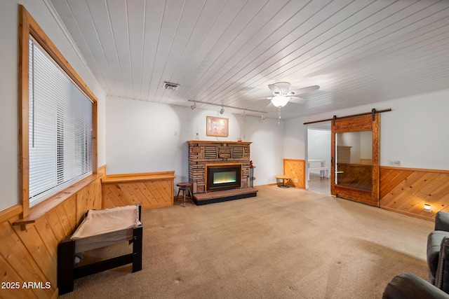 living room with a wainscoted wall, carpet floors, a stone fireplace, wood walls, and a barn door