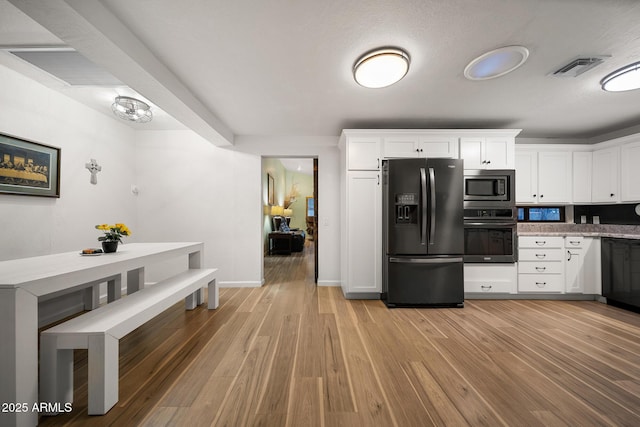 kitchen featuring oven, visible vents, black fridge, stainless steel microwave, and light wood finished floors