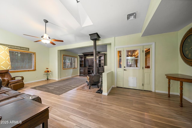 living area featuring visible vents, lofted ceiling with skylight, wood finished floors, ceiling fan, and a wood stove