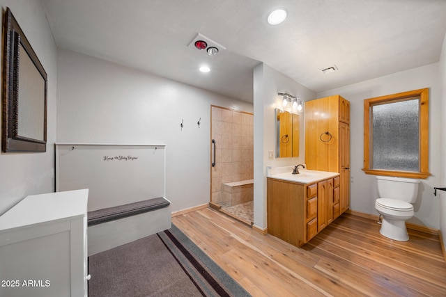 bathroom featuring tiled shower, toilet, wood finished floors, and vanity