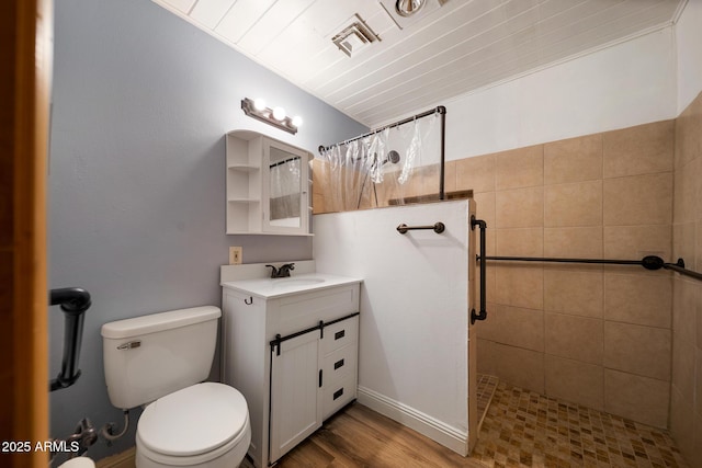 full bath with visible vents, toilet, a tile shower, wood finished floors, and vanity