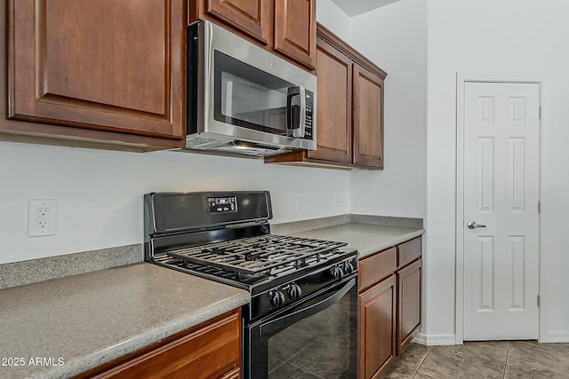 kitchen with stainless steel microwave, light tile patterned flooring, light countertops, and black gas range oven