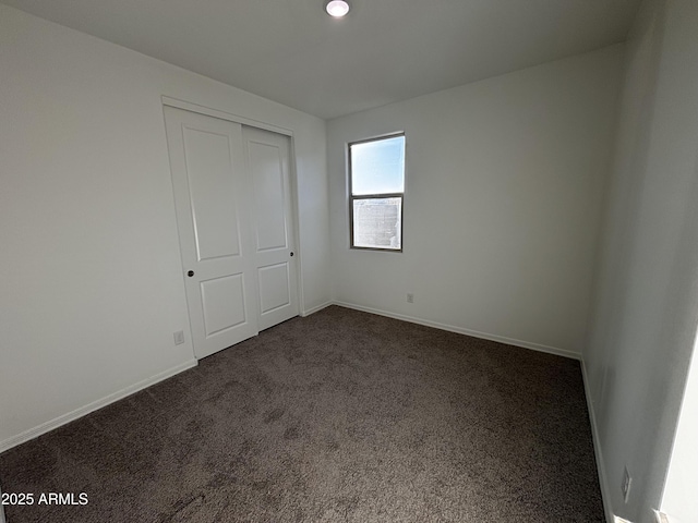 unfurnished bedroom with dark carpet and a closet