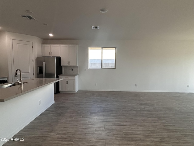 kitchen with white cabinetry, sink, dark hardwood / wood-style flooring, backsplash, and a center island with sink