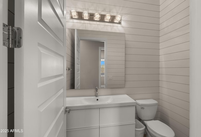 bathroom featuring toilet, vanity, and wood walls