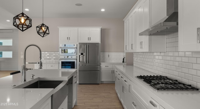 kitchen with pendant lighting, white cabinets, wall chimney range hood, and appliances with stainless steel finishes