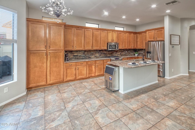 7252 E Nance St, Mesa, AZ 85207 - kitchen with stainless steel appliances, tasteful backsplash, light stone counters, a center island with sink, and brown cabinetry