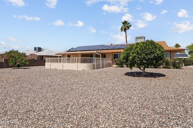 rear view of property with stucco siding, fence, and solar panels