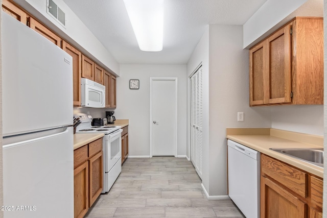 kitchen featuring sink, white appliances, a textured ceiling, and light wood-type flooring