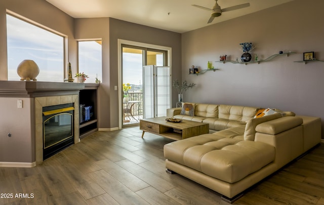 living room with a ceiling fan, baseboards, a tiled fireplace, and wood finished floors