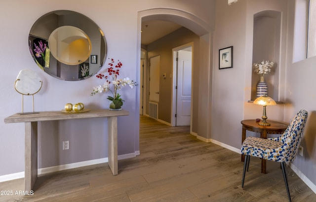 hallway with arched walkways, baseboards, and wood finished floors