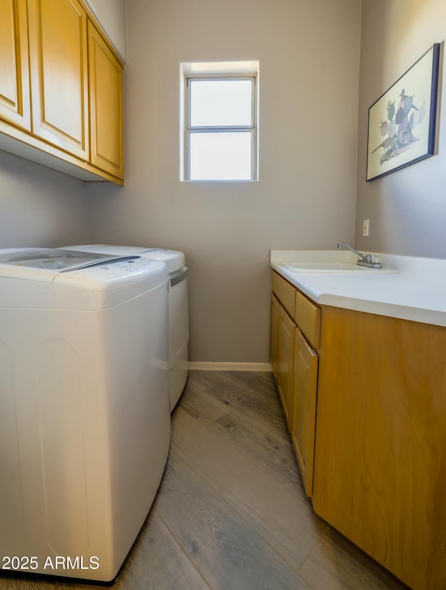 laundry area featuring light wood finished floors, cabinet space, washing machine and dryer, a sink, and baseboards