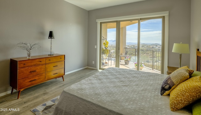 bedroom featuring baseboards, light wood-style flooring, a mountain view, and access to exterior