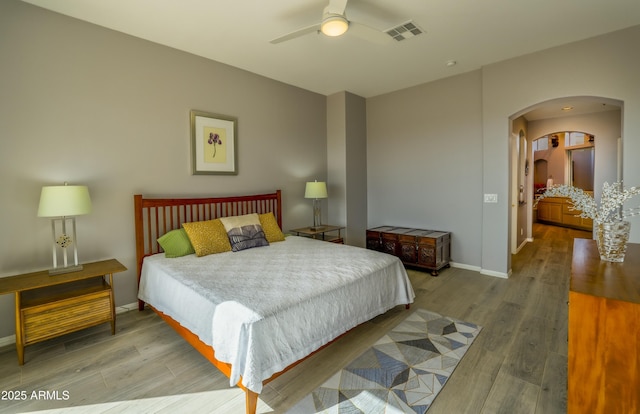 bedroom featuring arched walkways, wood finished floors, visible vents, and baseboards