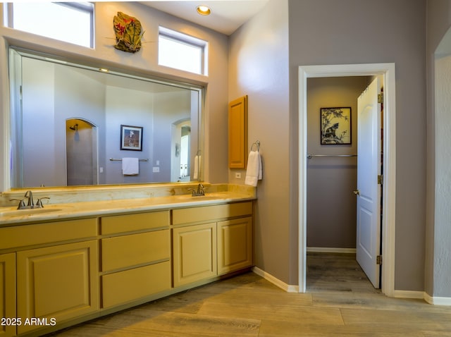 full bath featuring double vanity, baseboards, a sink, and wood finished floors