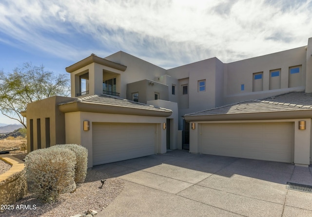 pueblo-style house featuring concrete driveway, a tiled roof, and stucco siding