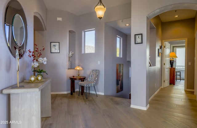 hallway featuring arched walkways, light wood-style flooring, and baseboards