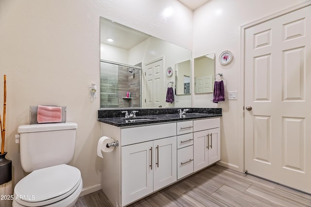 bathroom with a shower stall, baseboards, toilet, double vanity, and a sink