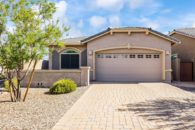 ranch-style house featuring fence, an attached garage, stucco siding, a tiled roof, and decorative driveway