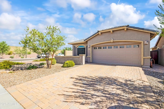 view of front facade with stucco siding, a tile roof, decorative driveway, fence, and an attached garage