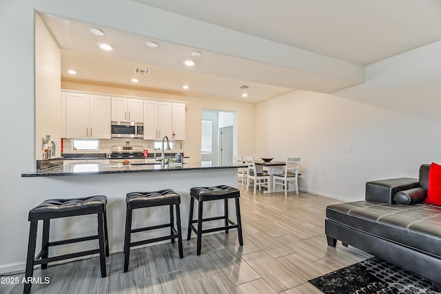 kitchen featuring visible vents, dark stone counters, stainless steel appliances, white cabinets, and a kitchen bar