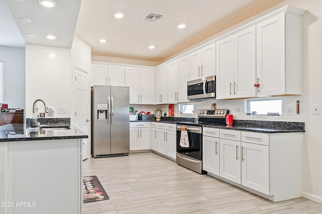 kitchen featuring dark stone countertops, visible vents, a sink, stainless steel appliances, and white cabinets