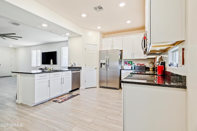 kitchen featuring visible vents, appliances with stainless steel finishes, a peninsula, white cabinets, and a sink