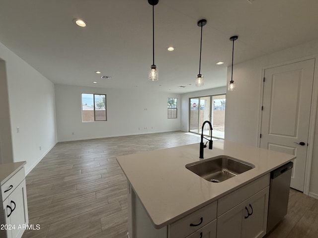 kitchen with sink, hanging light fixtures, light hardwood / wood-style flooring, stainless steel dishwasher, and a center island with sink