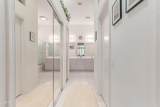 hallway with a textured wall, visible vents, and light tile patterned floors