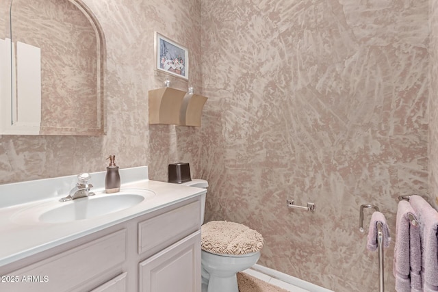 half bathroom with vanity, baseboards, wallpapered walls, and toilet