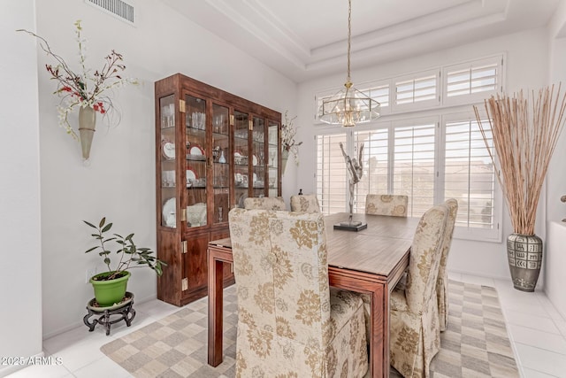 dining area with light tile patterned flooring, a notable chandelier, visible vents, and a raised ceiling